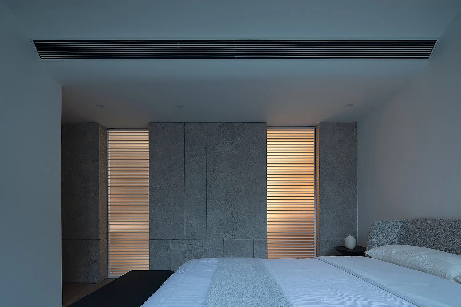 Spacious minimalist bedroom featuring concrete walls, wooden floor, and simple furniture.