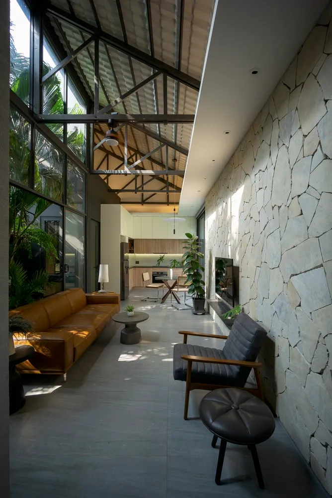 Modern industrial living room with concrete walls and floor, featuring a leather sofa and armchairs, and large windows with g