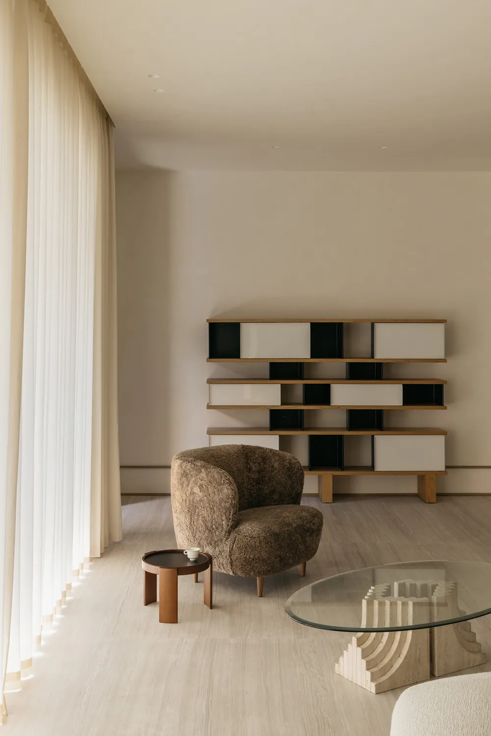 A minimalist living room featuring muted-tones furniture and shelves.