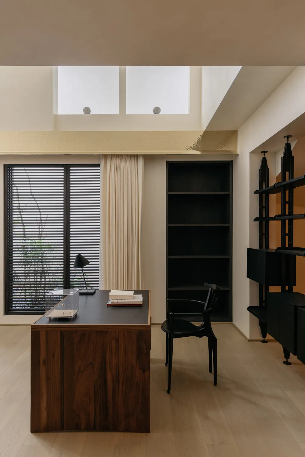 Minimalist office space featuring a wooden desk, black chair, and bookshelf