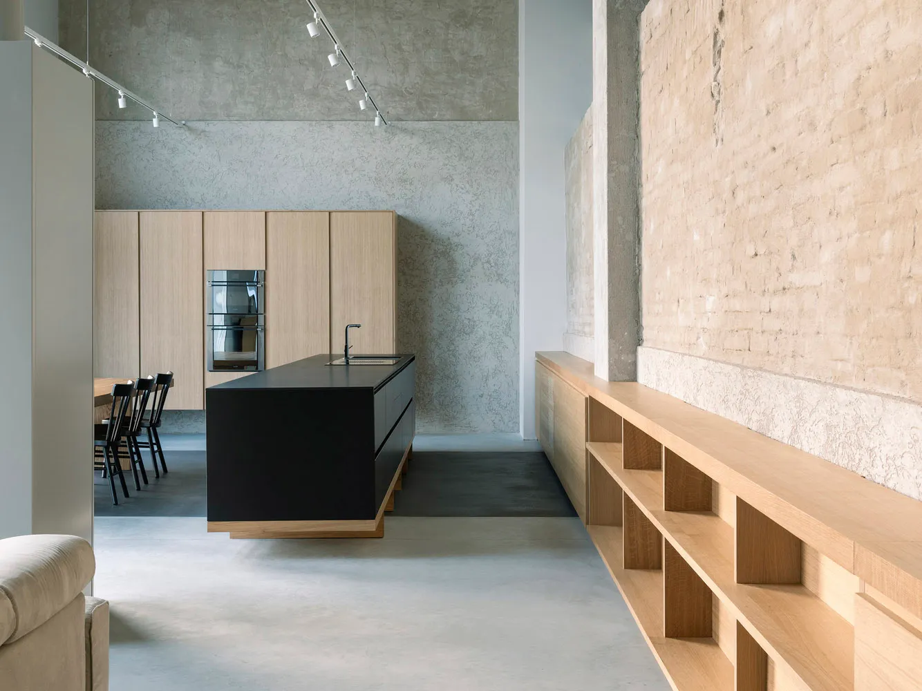 Modern minimalist residential kitchen featuring a black island with sink, wooden cabinetry, and exposed brick walls.