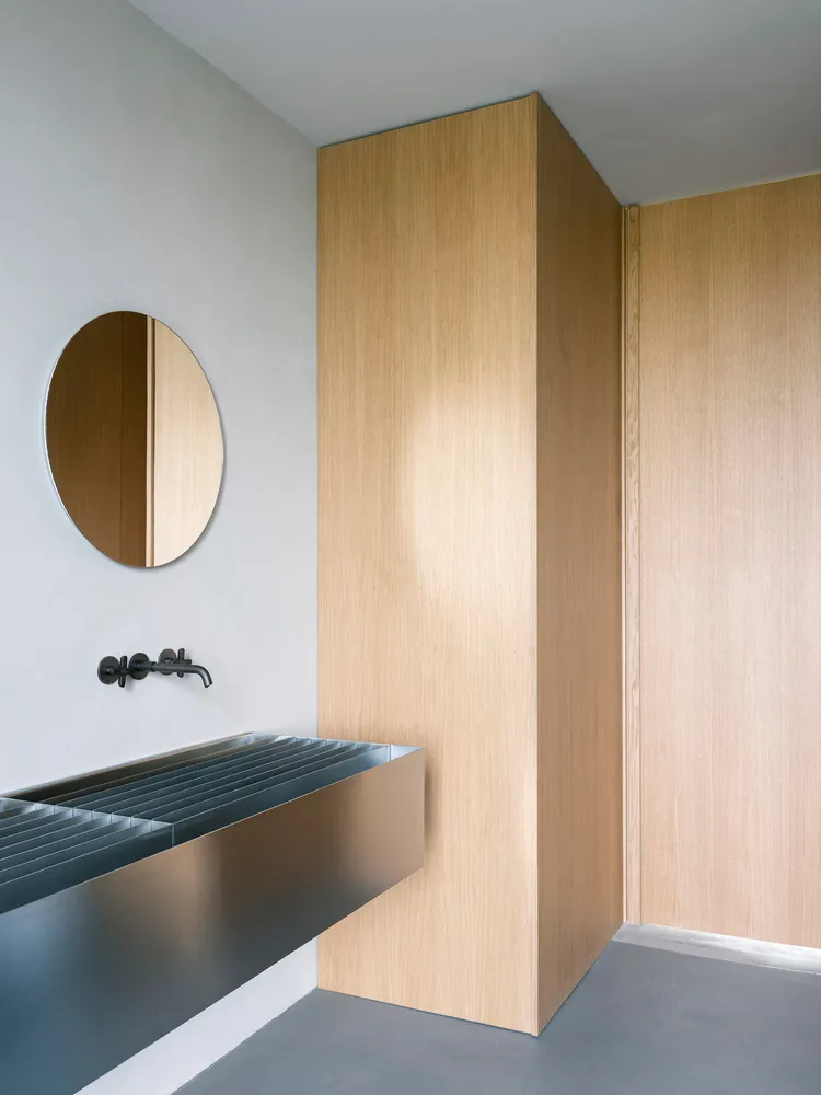 Modern minimalist bathroom with wooden walls and a circular mirror.