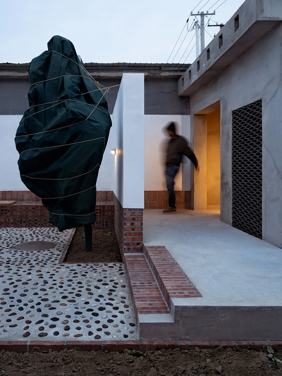 A concrete exterior with a covered tree and a person walking through a doorway.