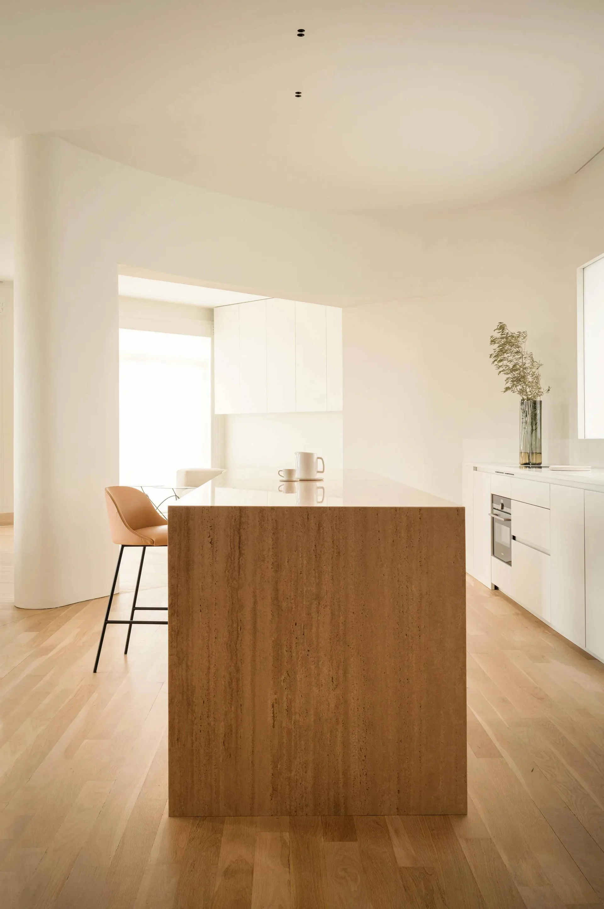 A minimalist kitchen with white cabinets, wooden flooring, and a large island.