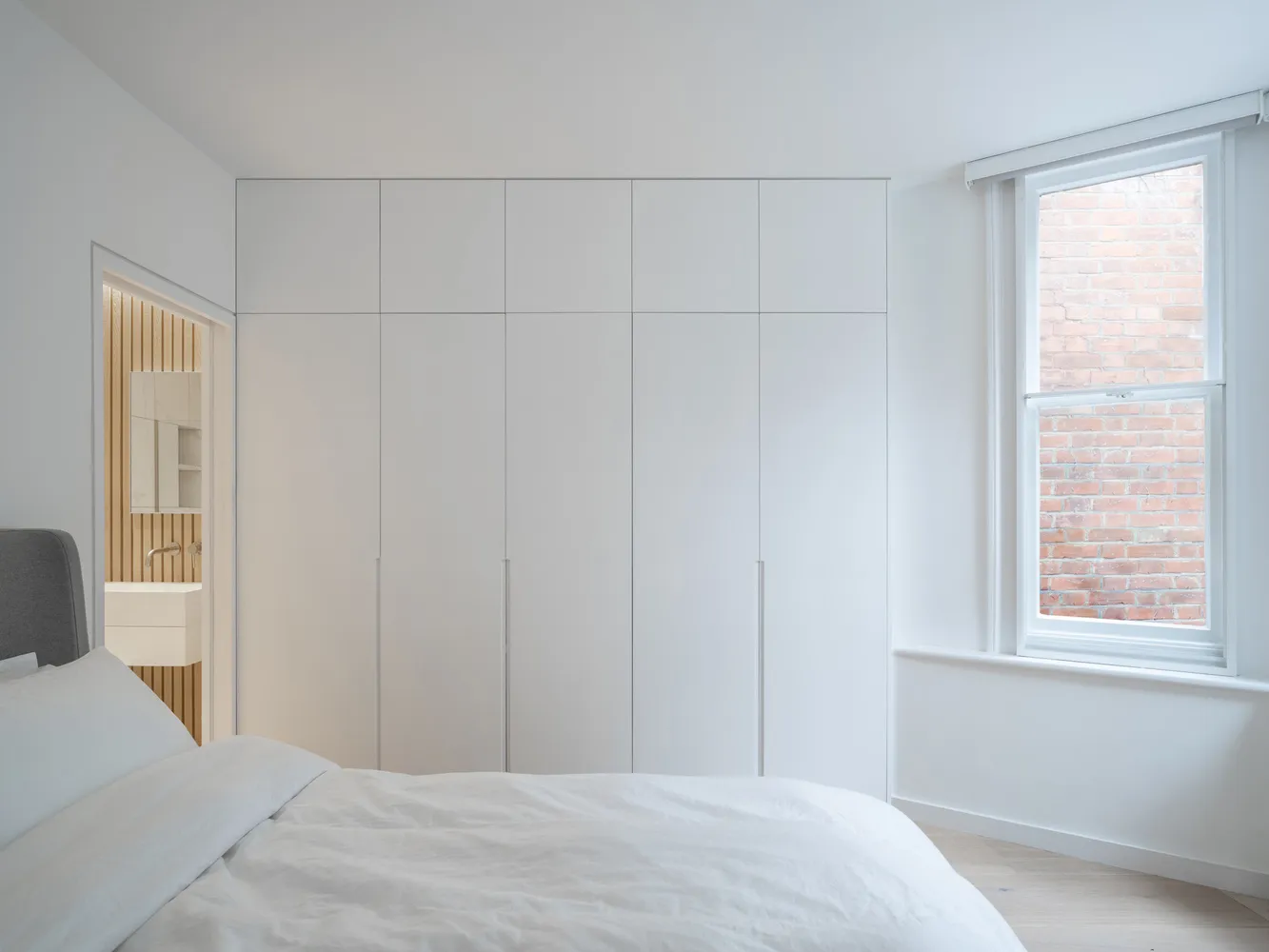 A minimalist bedroom with a white bed and a large white wardrobe.