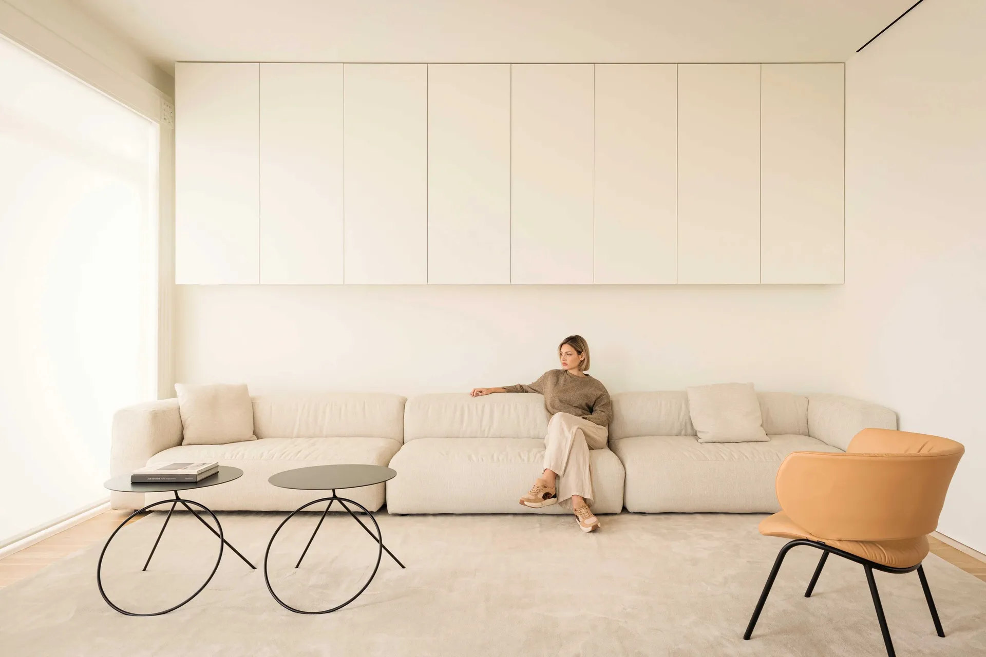 A minimalist living room with a neutral-toned sofa, coffee tables, and a modern chair in a contemporary space.