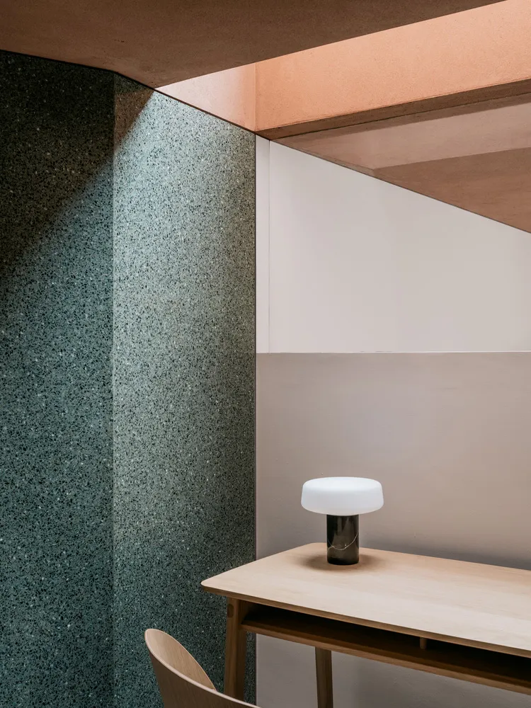 A minimalist office space featuring a desk made of wood with a modern, round lamp and a wall with a combination of terrazzo a
