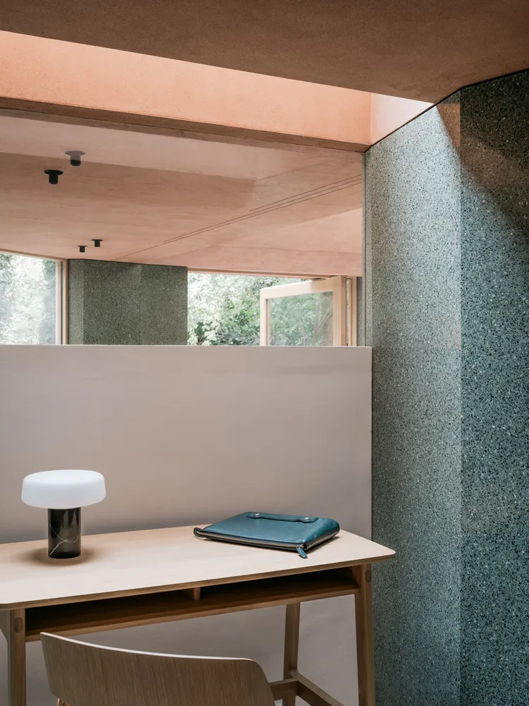 A modern home office featuring a sleek desk, a minimalist lamp, and a leather notebook against a concrete backdrop.