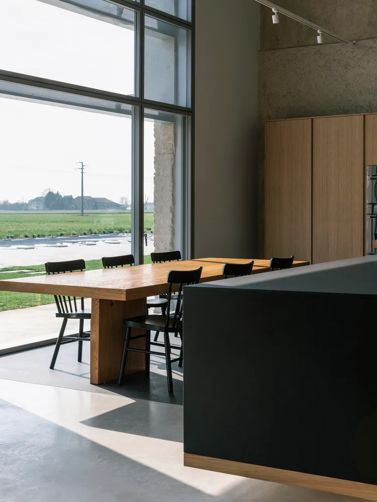 Modern dining room with wooden furniture and large windows overlooking green fields.