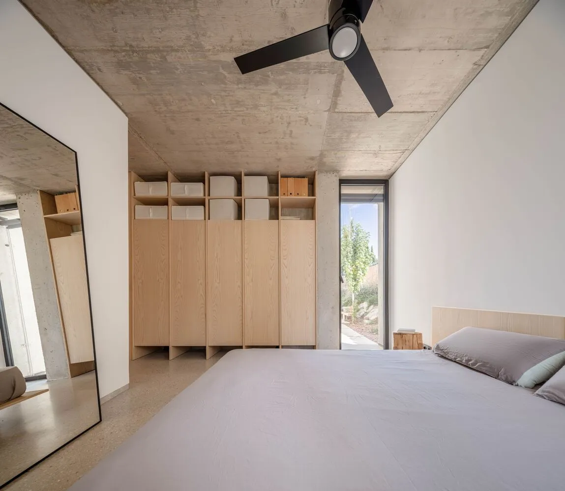 Modern minimalist bedroom with concrete stone cabinets, wooden bed and headboard, and mirror.