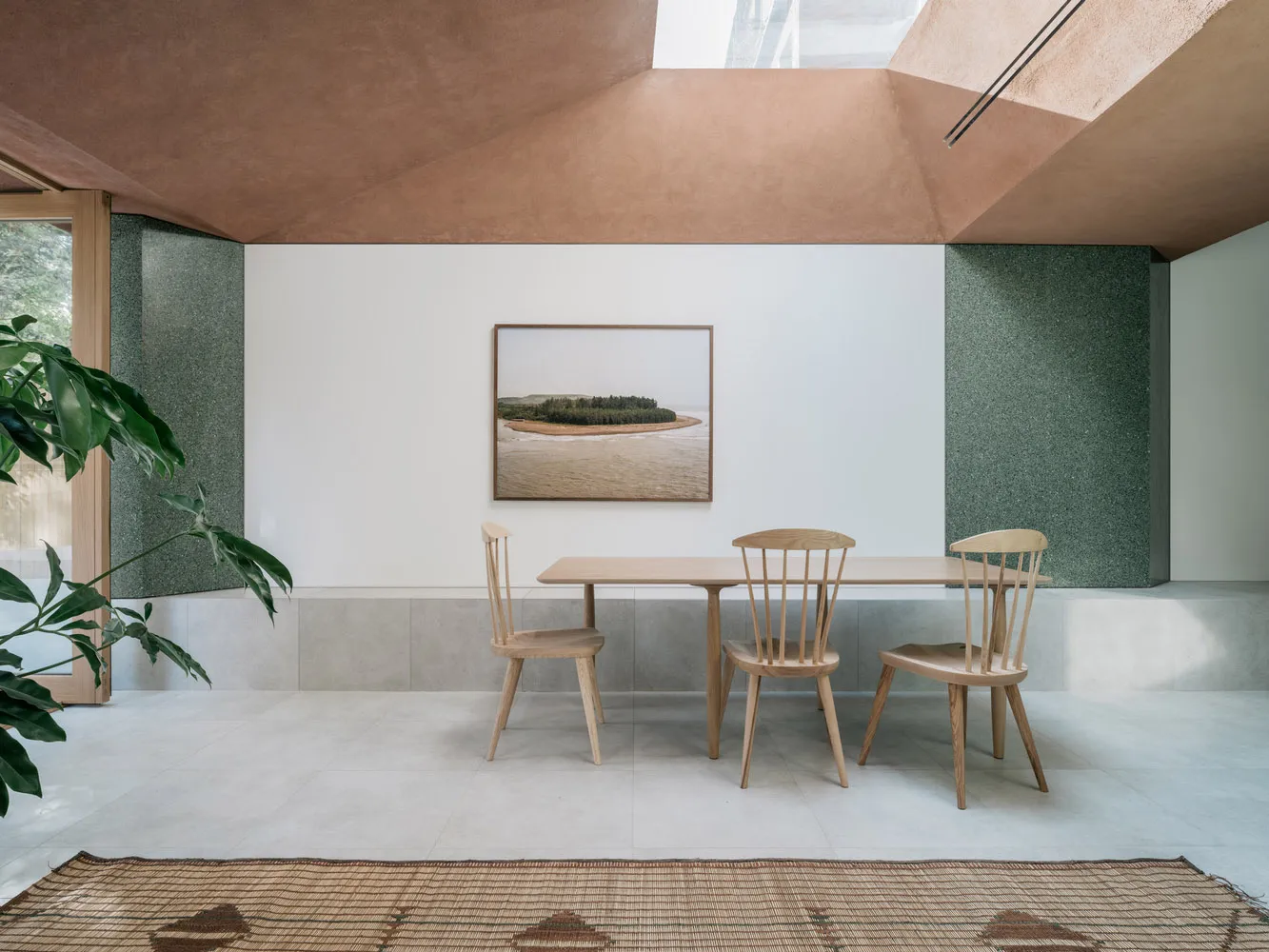 A minimalist interior with a wooden table and ceramic tiles, featuring a light fixture and a framed photograph.