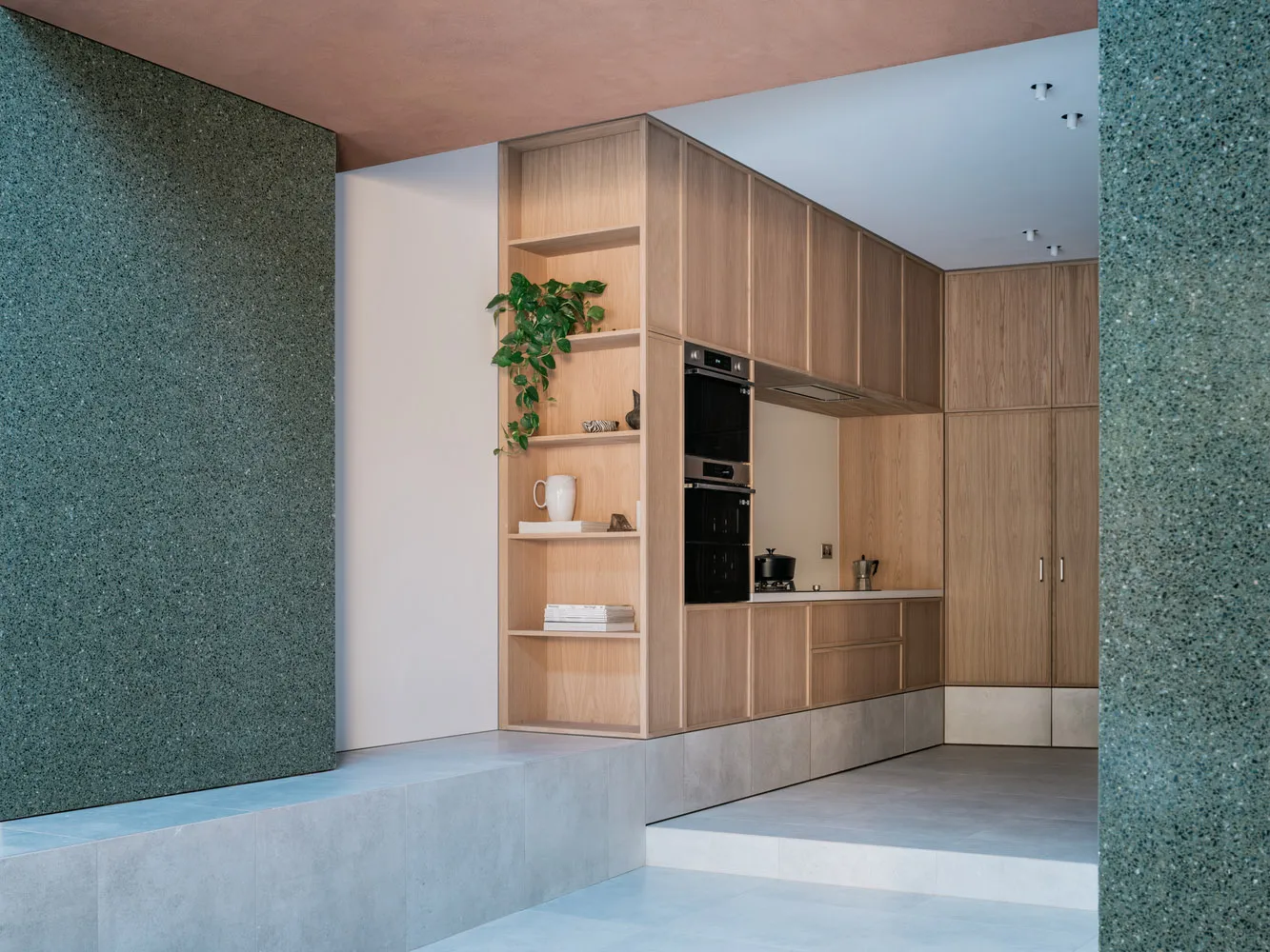 Modern kitchen interior with wooden cabinets and shelves, green plant, and white appliances.