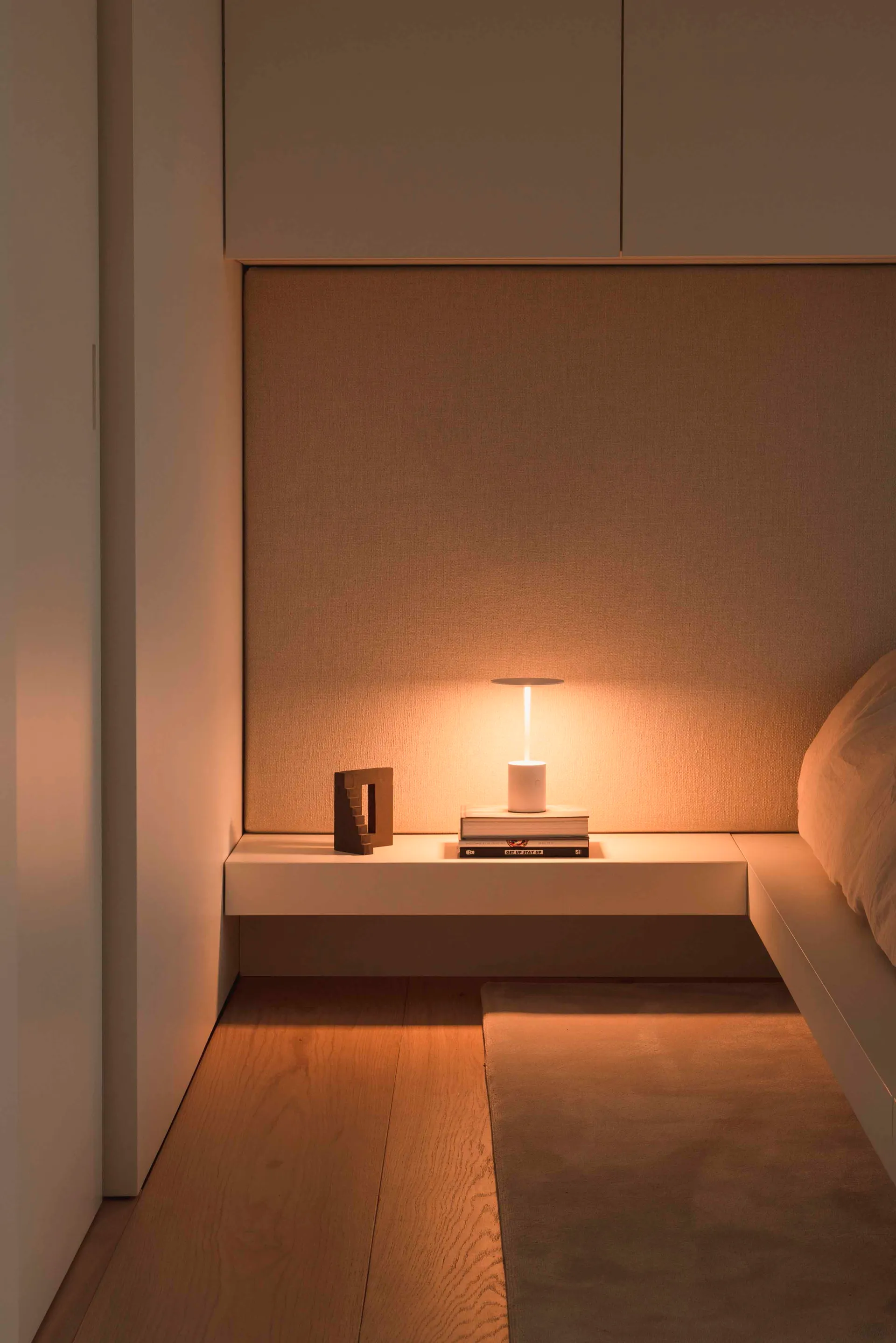 A minimalist bedroom with white furnishings, wood flooring, and overhead lighting.