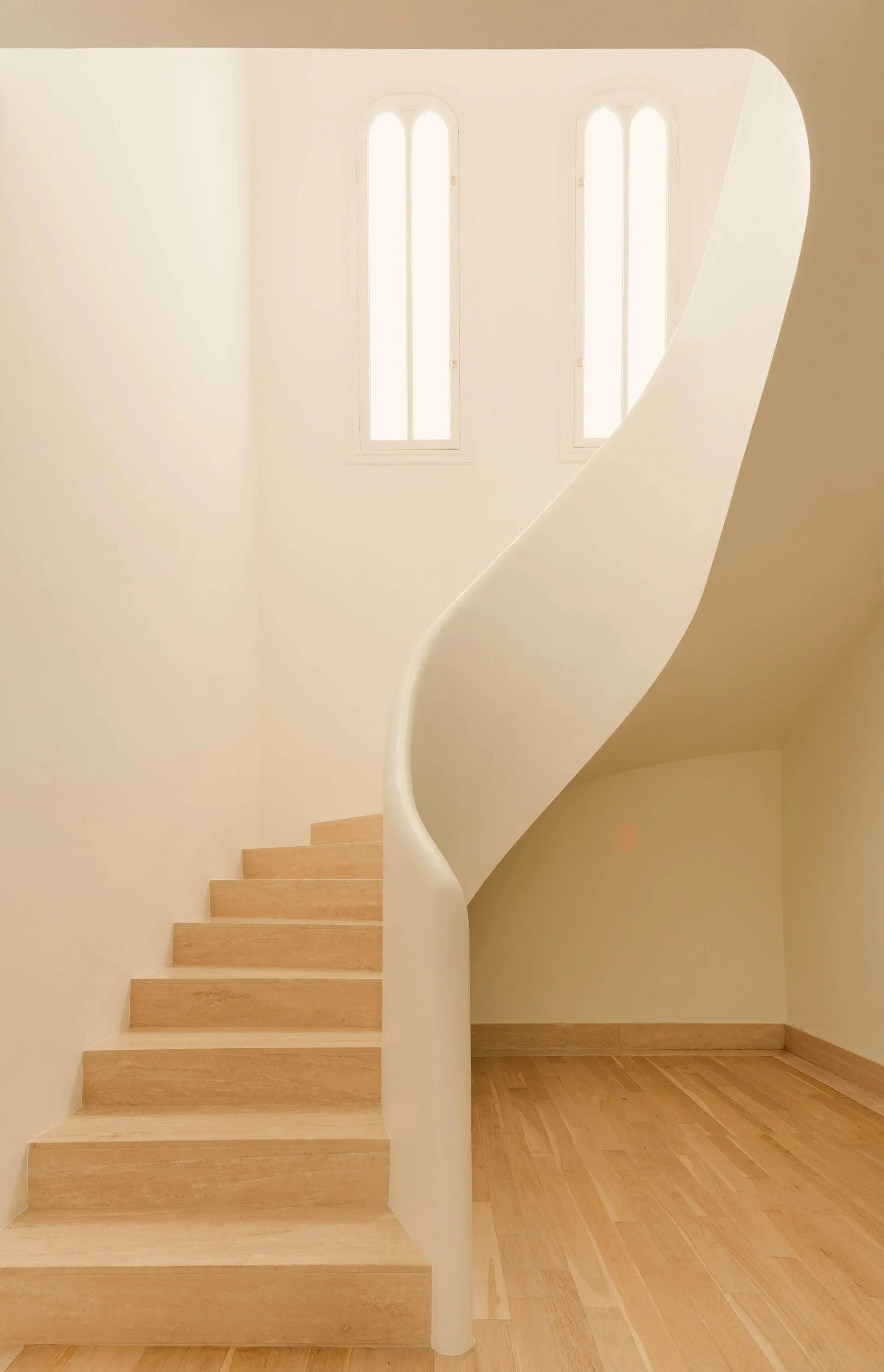 A modern interior staircase with wooden steps and railings, featuring an archway and natural light.