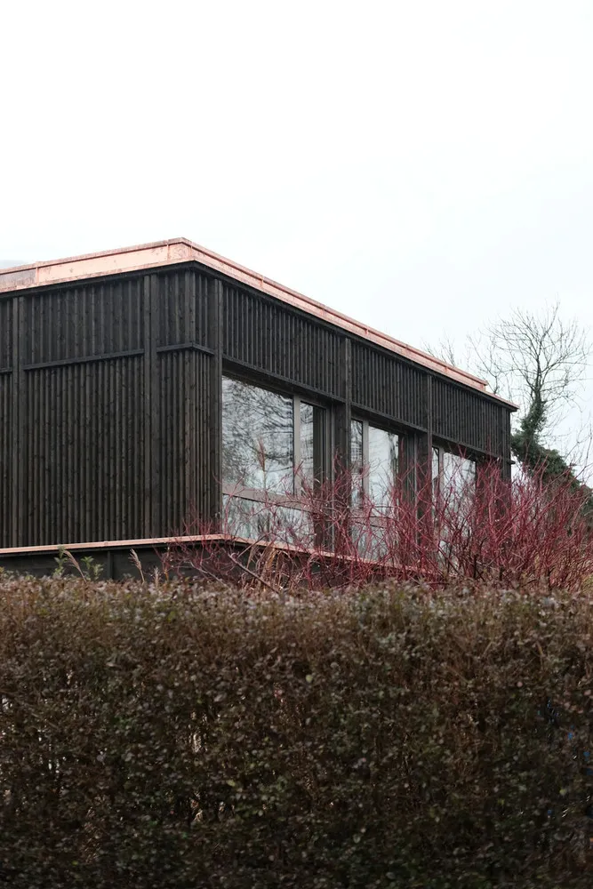 A modern building with black cladding and a copper roof, viewed from the side.