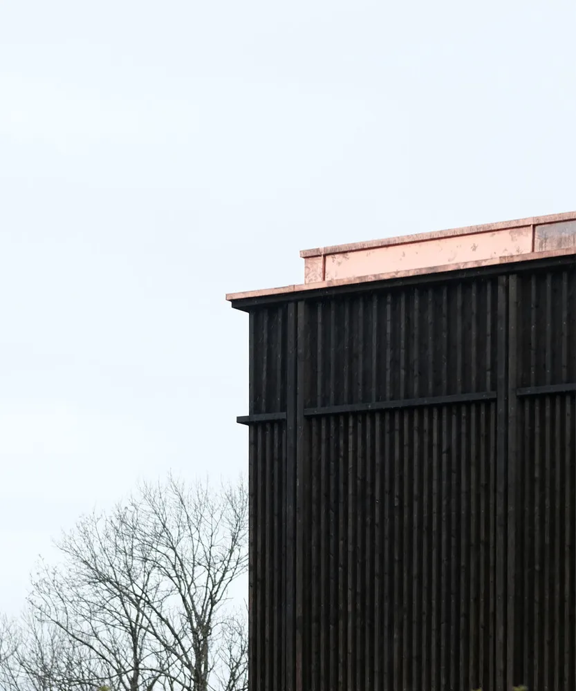 A modern building with dark siding and a copper-colored roof