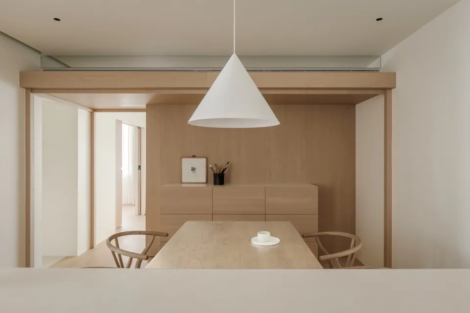 A minimalistic dining room with a wooden table and chairs under a white pendant light.