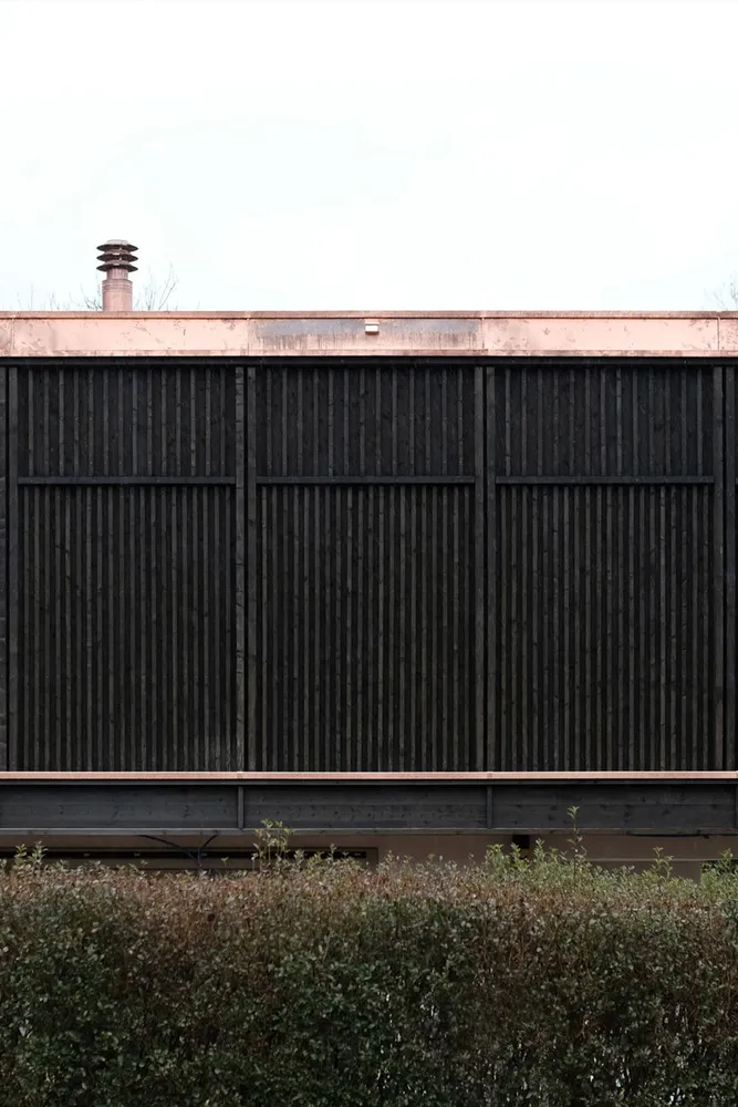 A modern arbor with a dark wooden slat design and a copper roof.