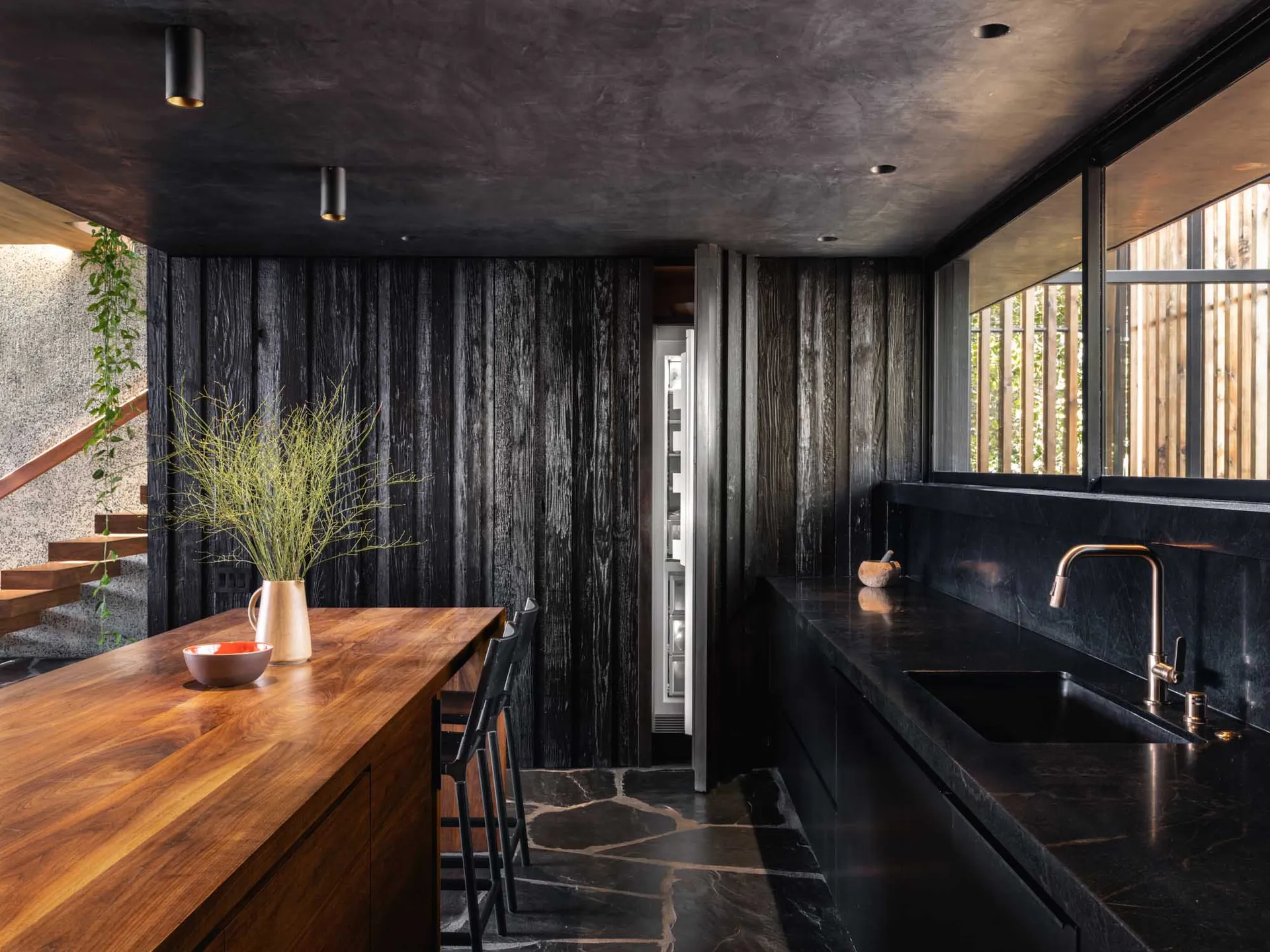 Modern kitchen featuring black stone countertops with a wooden island and green plant on top.