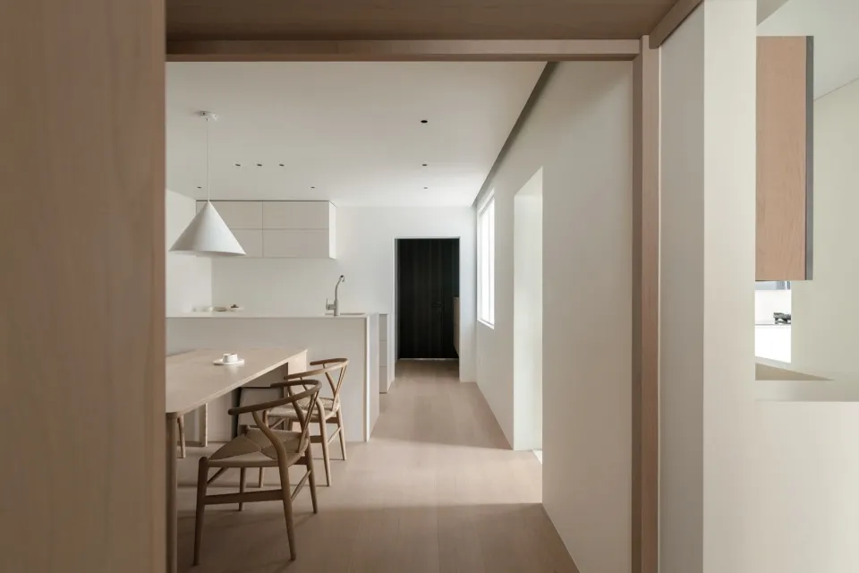 Minimalist kitchen with wood flooring, white cabinets, and a dining table.
