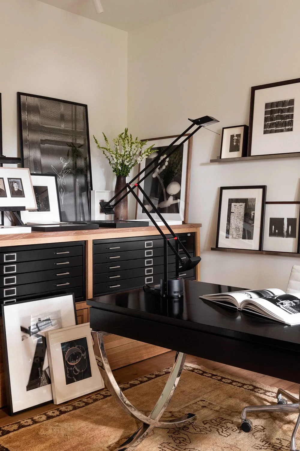 Industrial-style office with metal desk and black filing cabinet inside a room featuring multiple framed photographs on the w