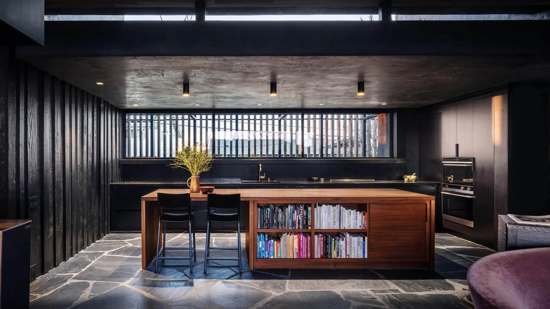 現代簡約廚房，木質中島搭配石材地板，設有書架與吧台椅。
