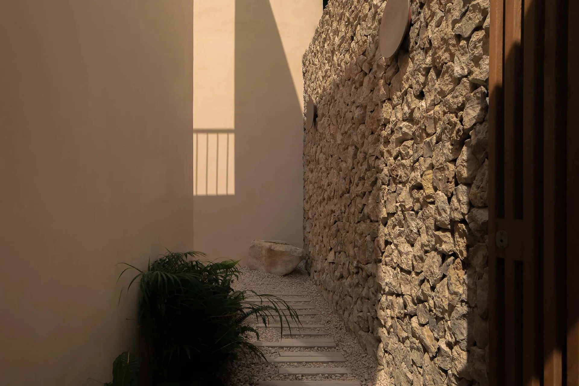 A narrow stone-walled hallway with a plant and sunlight coming through a window.