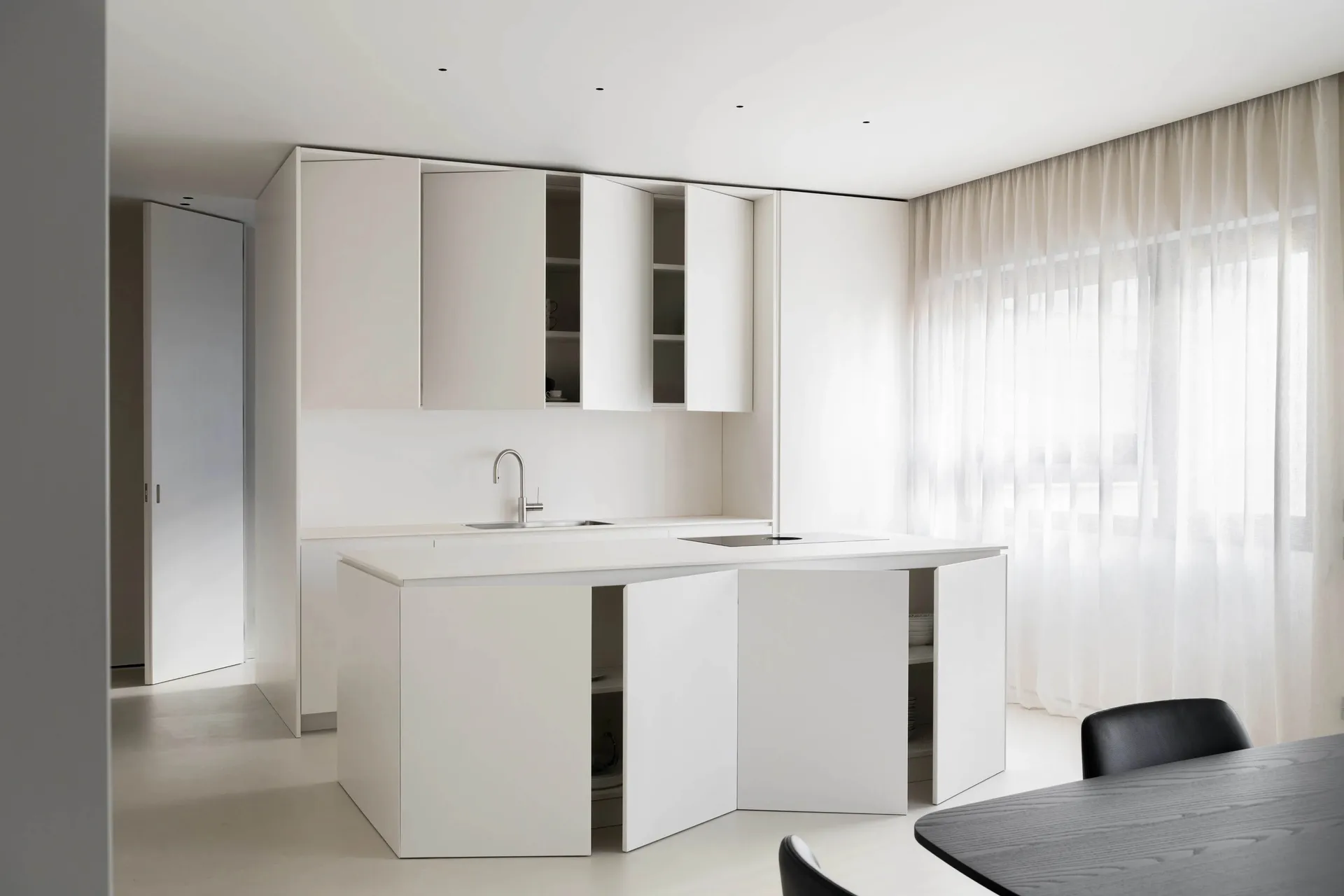 Modern, minimalist kitchen with white cabinets and countertops, featuring a sleek design and a small window.