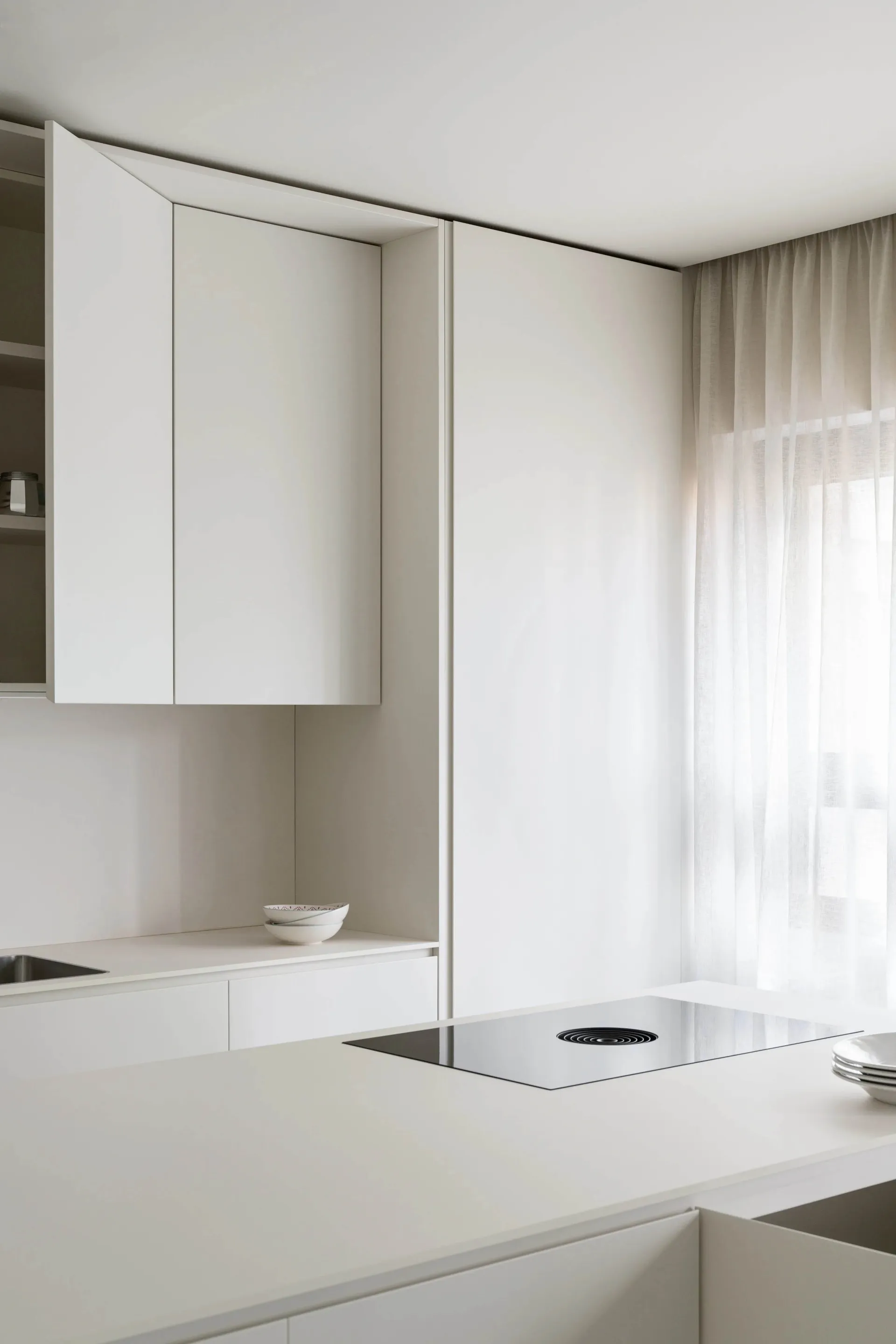 Modern minimalist white kitchen with glass cabinets and stainless steel appliances.