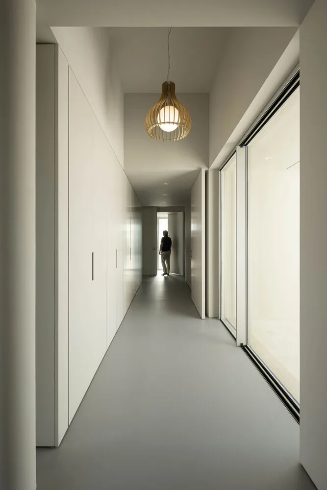 A modern corridor with white plaster walls and wooden pendant light.