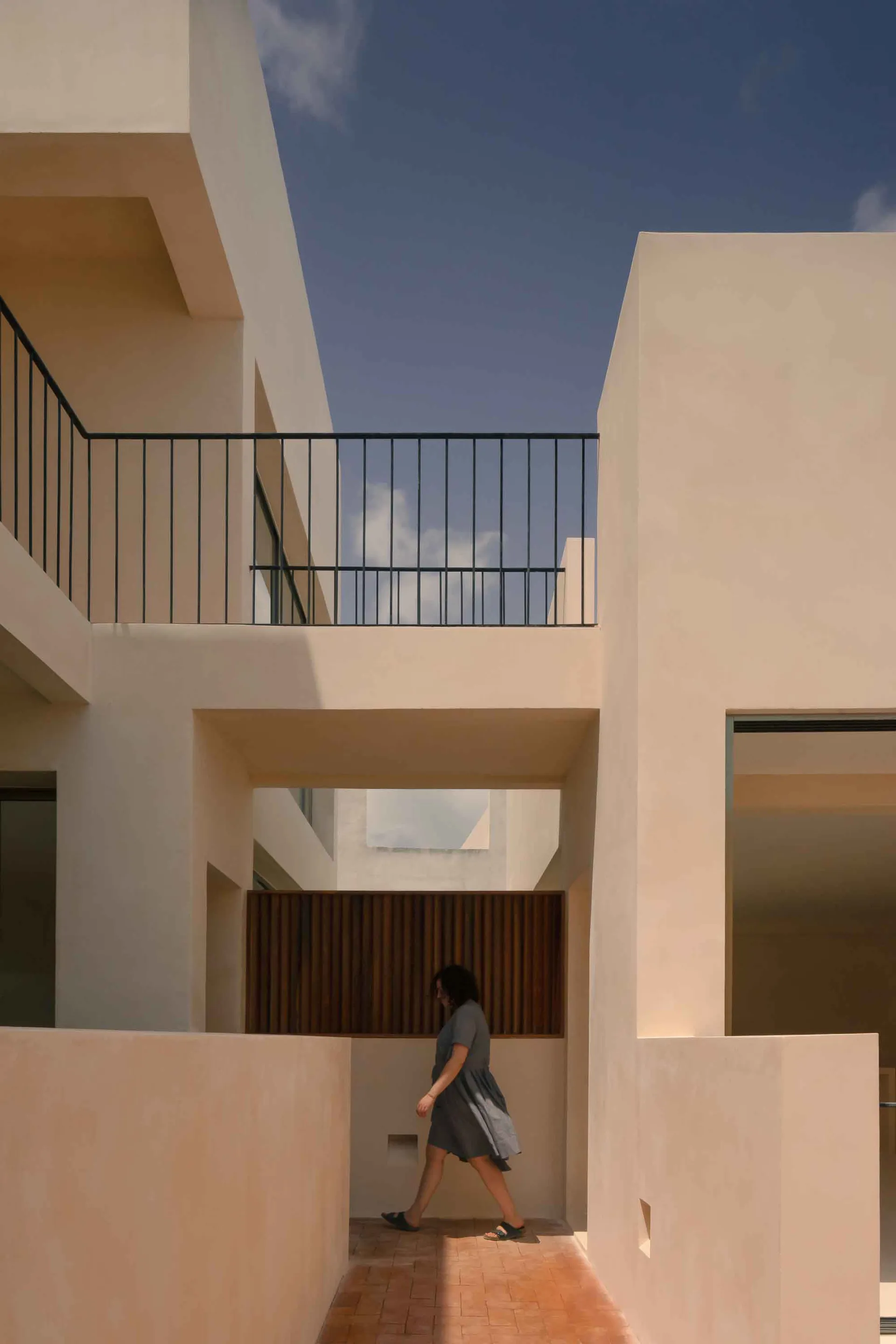 Person walking through a modern residential exterior featuring sandstone, concrete, and glass materials.