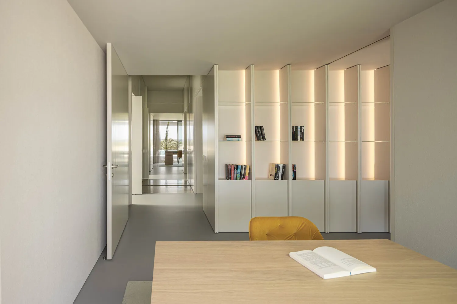 A minimalist office space featuring a metal and glass bookshelf with integrated lighting.