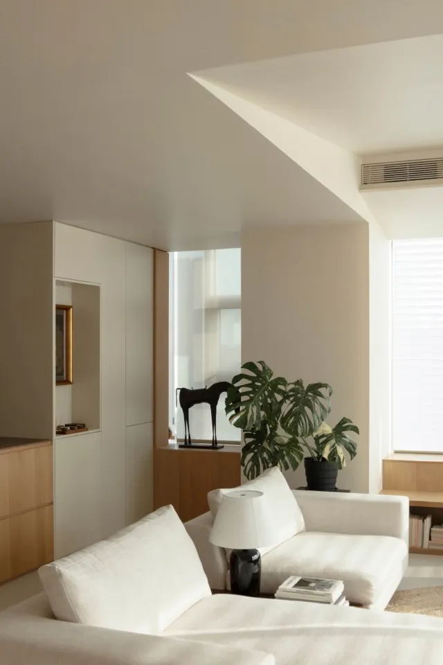A minimalist living room with white furniture, a black horse statue, and a potted plant.