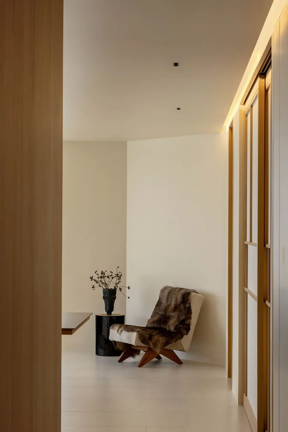 A minimalist corridor interior with neutral-toned walls and hardwood floors, featuring a single cushioned chair draped with f