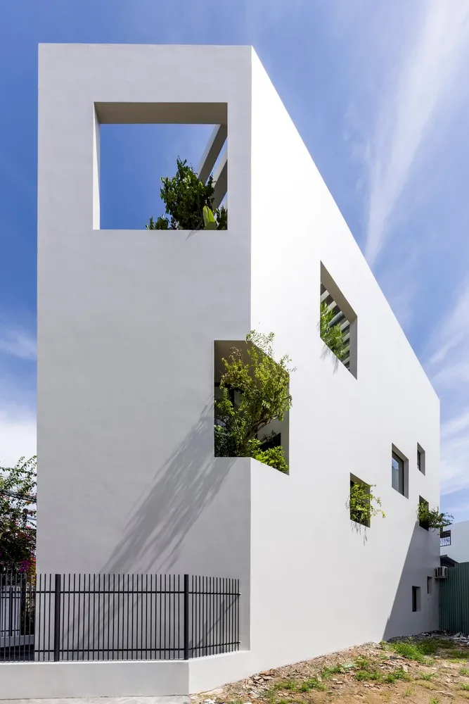 A modern, exterior view of a white-box house with concrete walls and large windows.