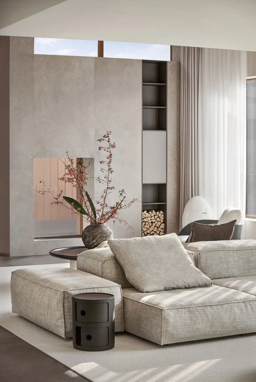 A modern minimalist living room with a concrete fireplace, fabric furniture, and glass shelves.