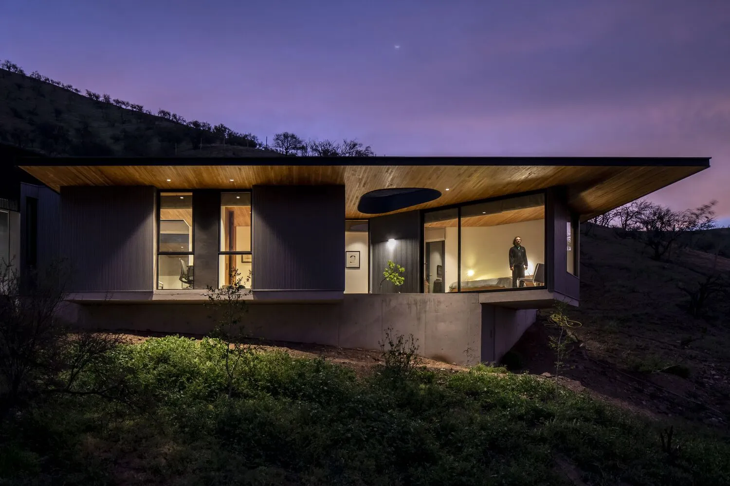 Modern residential house exterior during twilight with wooden and concrete exterior and large glass windows.
