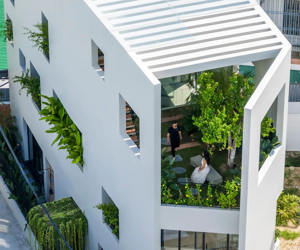 一座現代白色建築，窗台擺放綠植，周圍環繞茂密綠意。