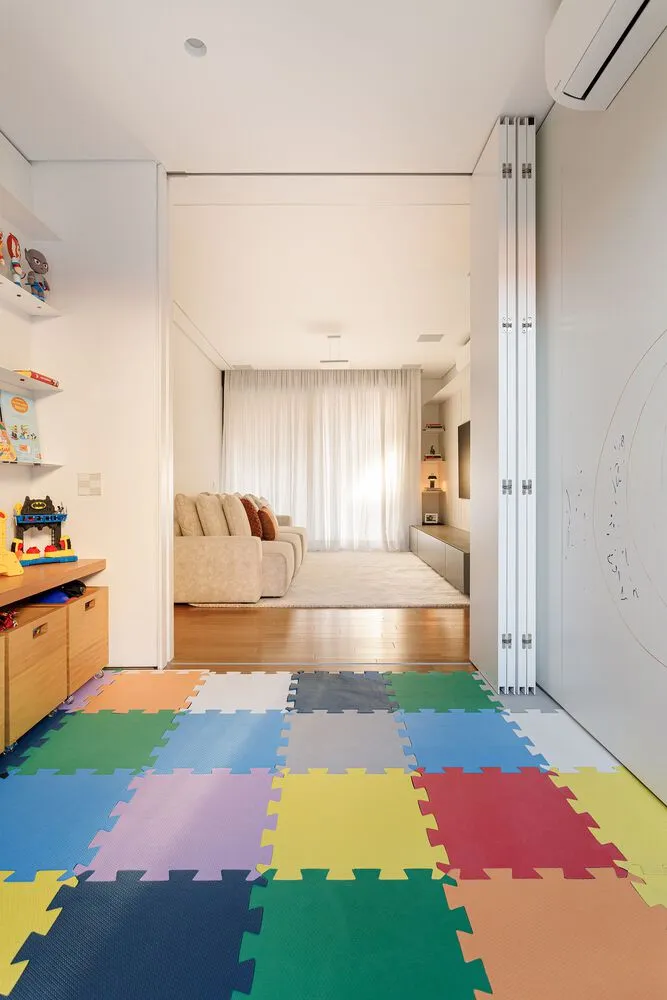 A colorful playroom with a geometric pattern on the floor, white walls, and a tan sofa with red and brown pillows.