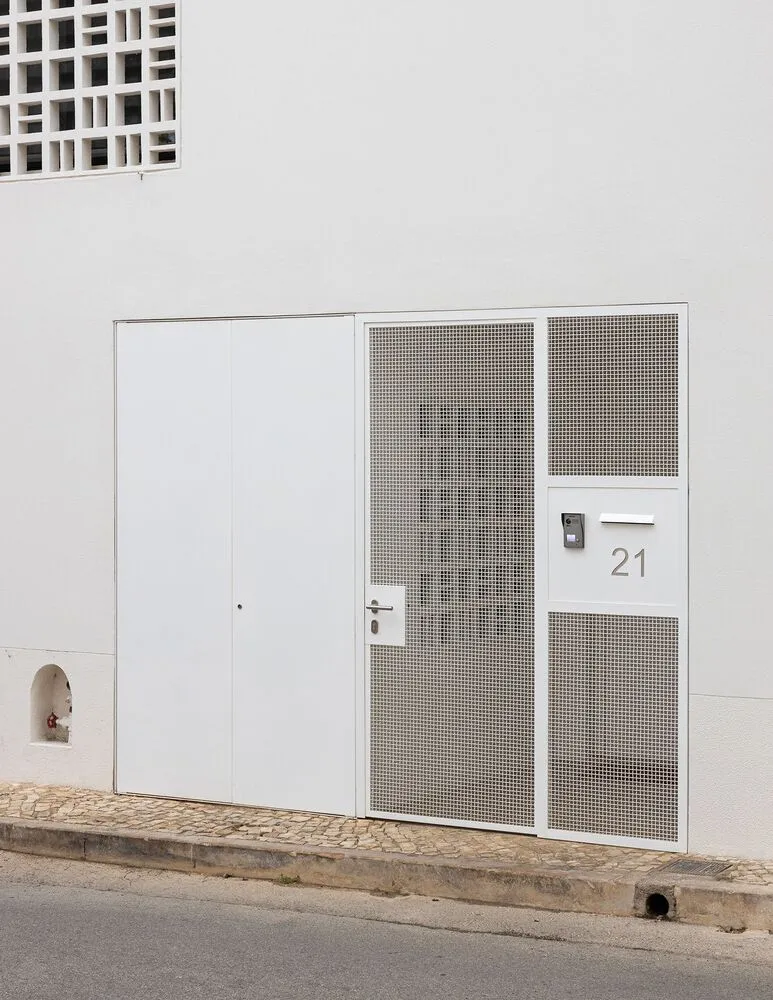 A modern building entry door with a metallic grid pattern and concrete wall in white color.