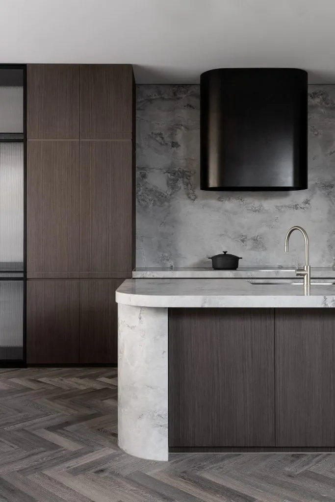 Modern industrial kitchen with a marble countertop, wooden cabinets, and concrete walls.