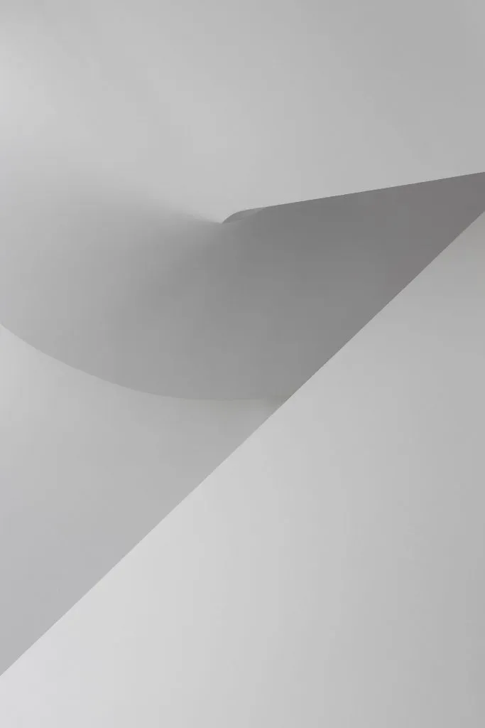 簡約白色空間，帶有曲面牆與平面上投射的陰影。