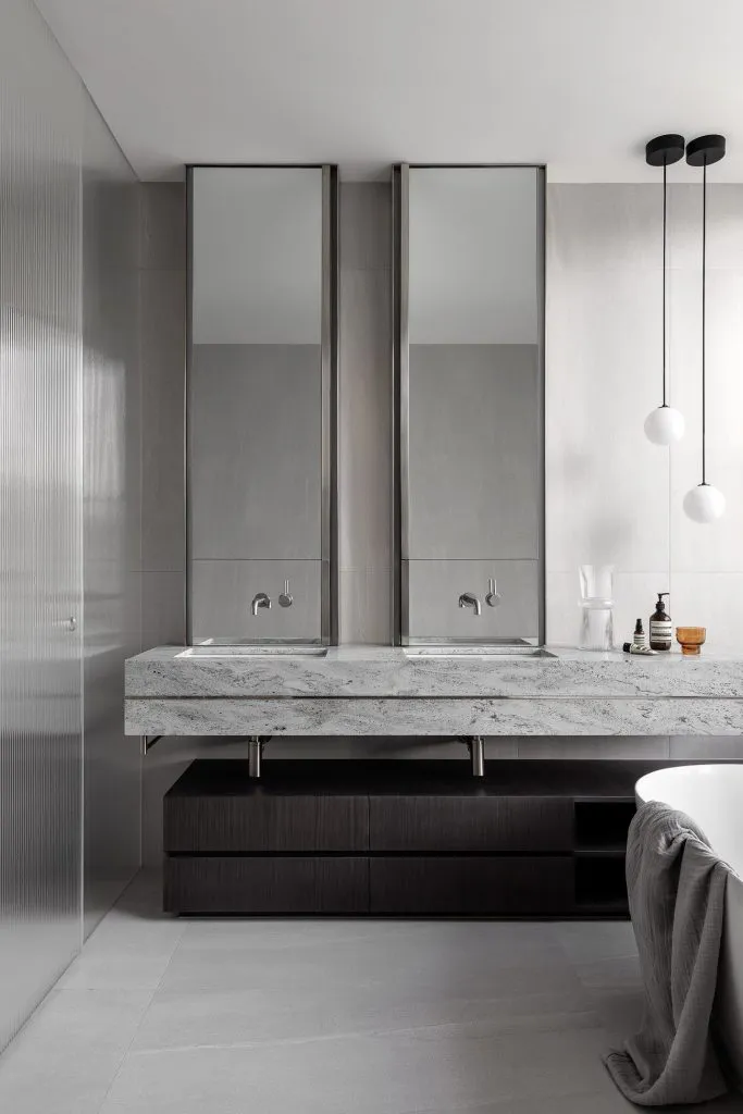Modern, minimalist bathroom featuring a granite countertop with two sinks and tall mirrors.