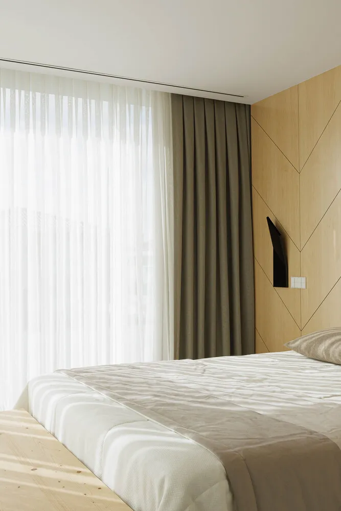 Modern minimalist bedroom with a bed covered in a fabric comforter and a wooden headboard