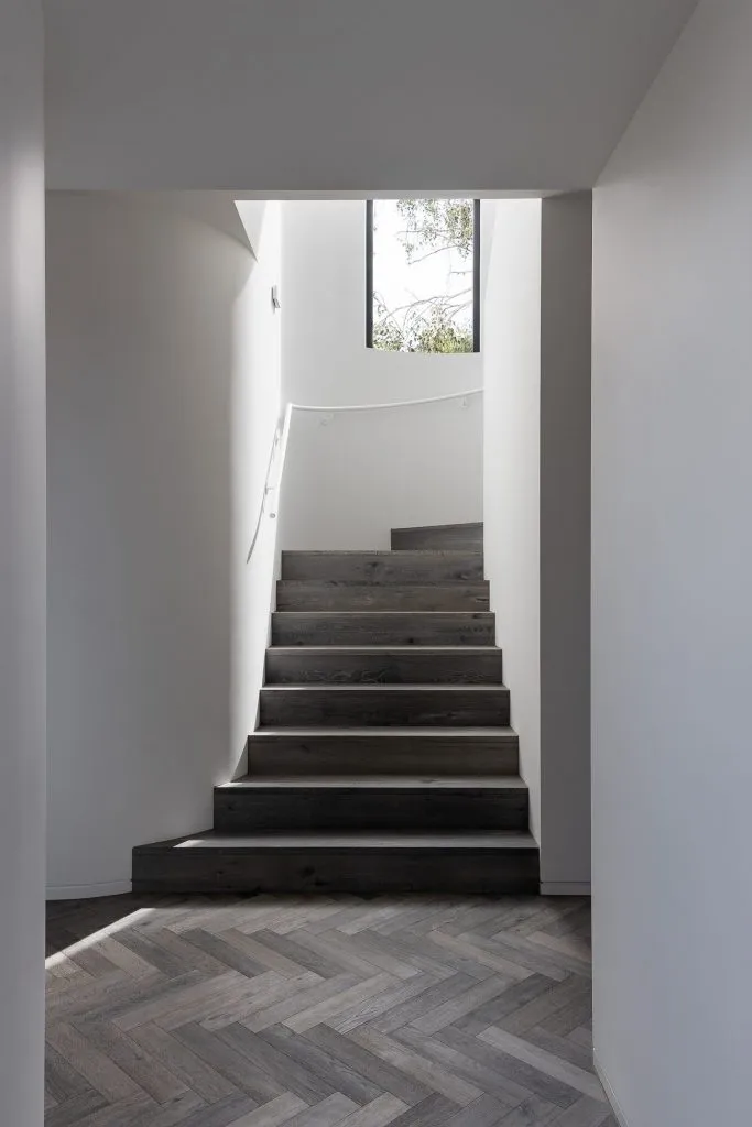 A modern staircase with white lighting fixtures and wooden steps, set against white walls.