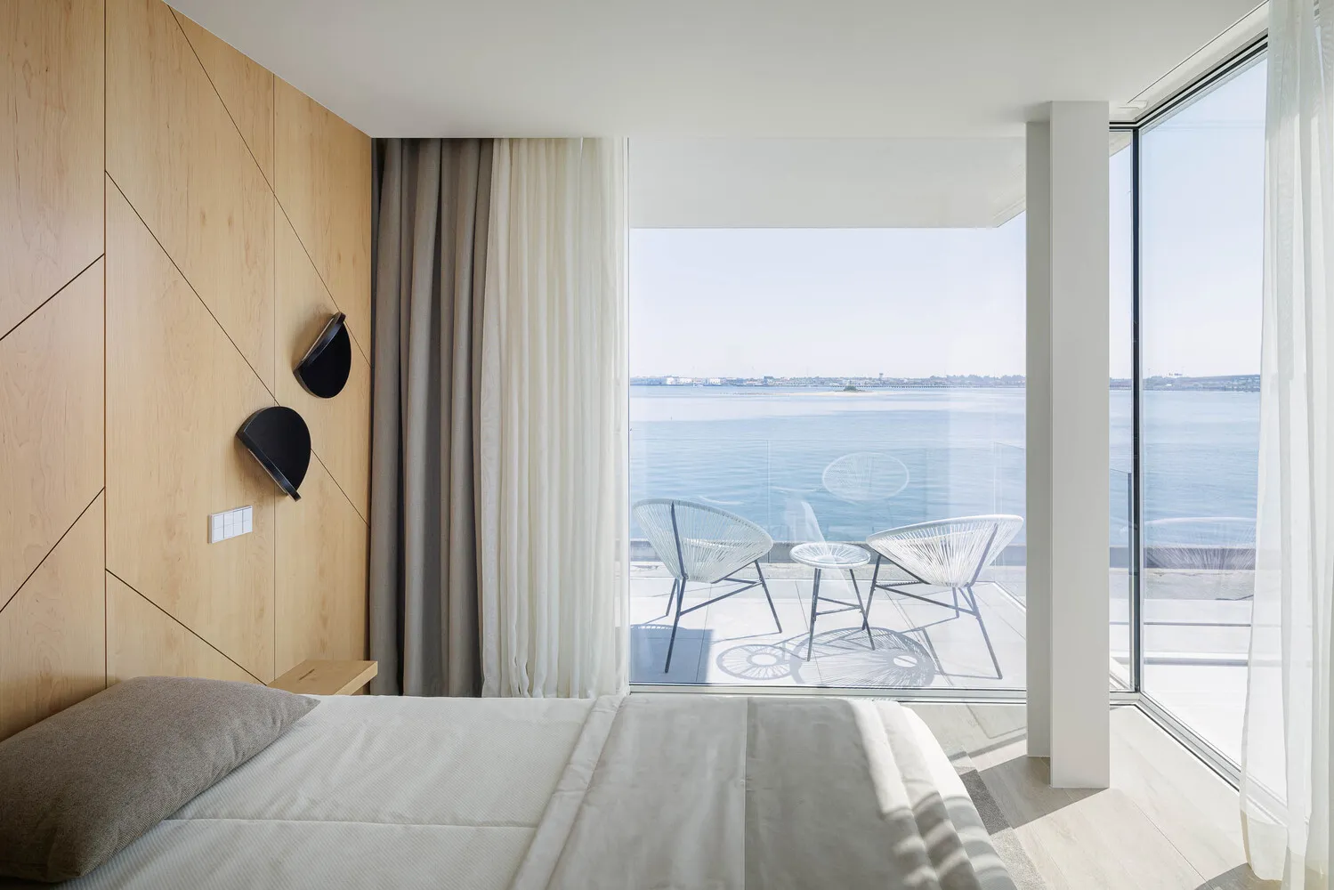 Modern minimalist bedroom with glass walls and a view of the sea.