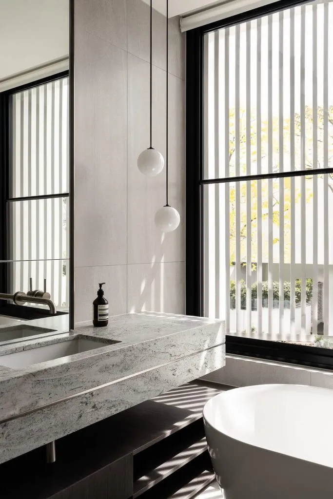 Modern bathroom interior featuring granite countertop and sink with vertical blinds and natural lighting.