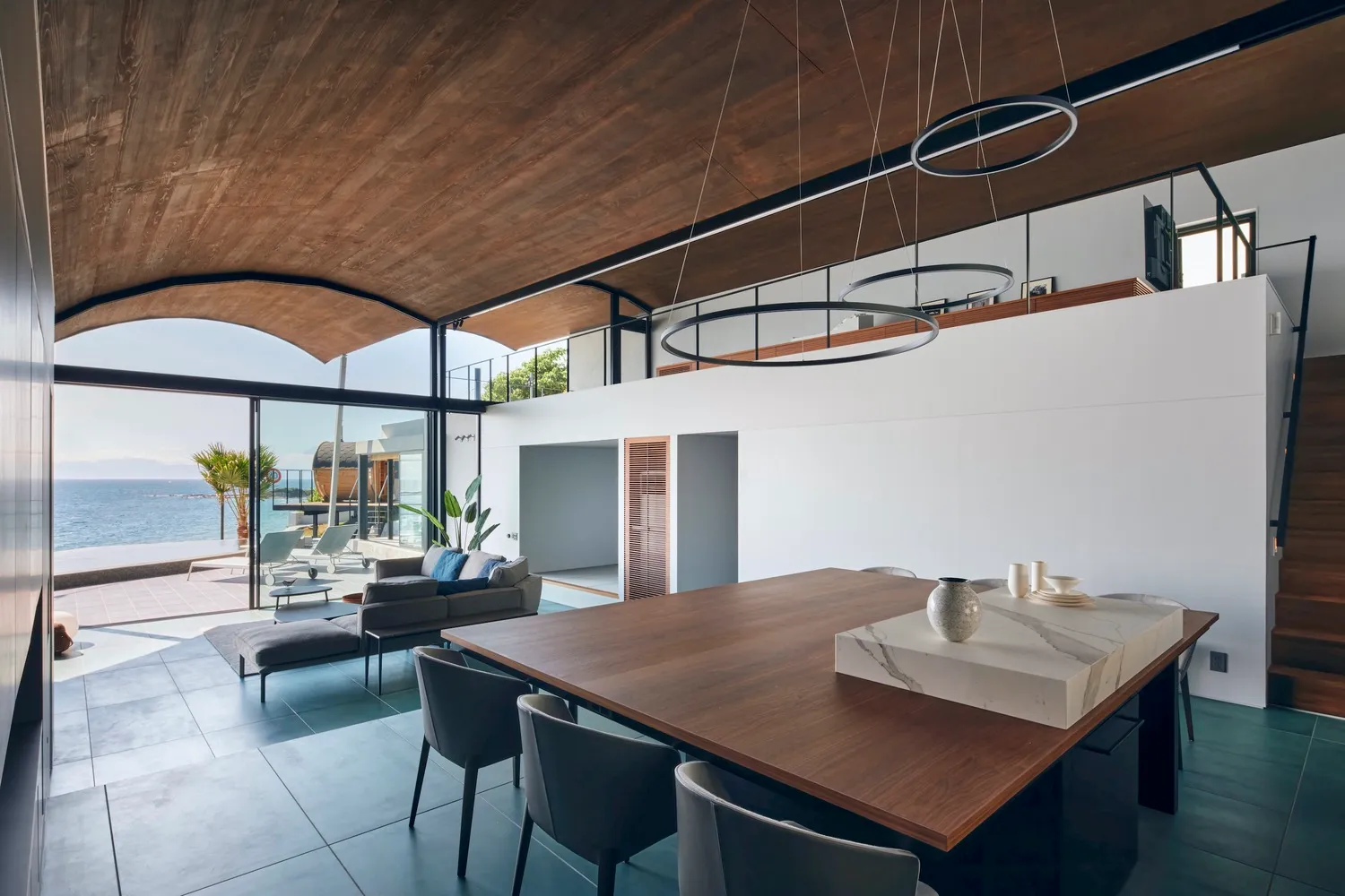 Modern minimalist living room with concrete floor and furniture, large windows with outdoor view of the sea, and minimalist d