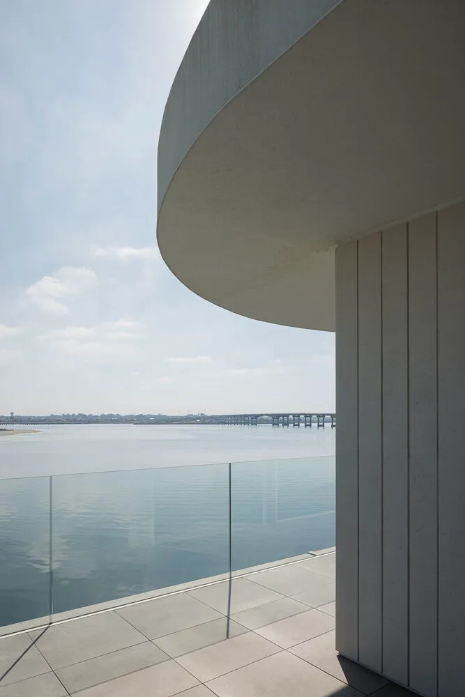 Modern residential balcony featuring concrete flooring and glass balustrade overlooking calm water.