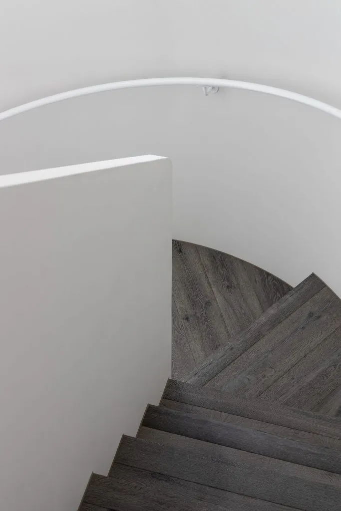 Modern wooden stairs with a white, curved wooden handrail and white walls.